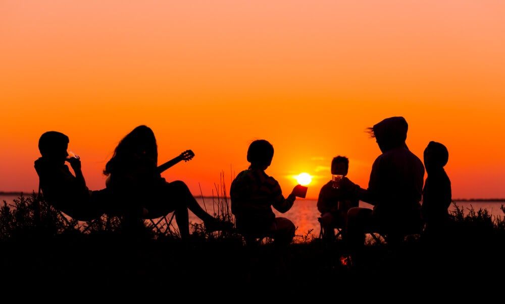 group of outdoor goers sitting on beach at sunset
