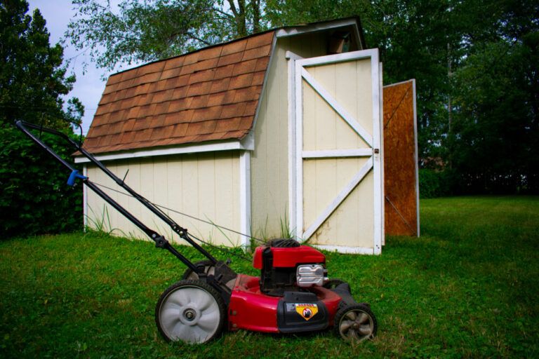 black and red lawn mower with shed in background