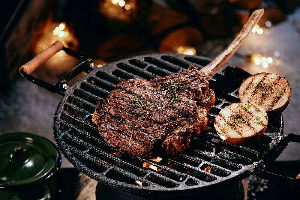 delicious looking tomahawk steak and onion getting grilled at night