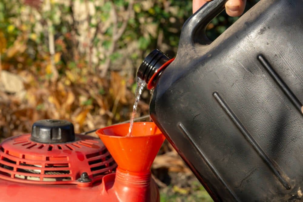 carefully pouring gasoline into the lawnmower tank using a funnel. overfilled oil in lawn mower
