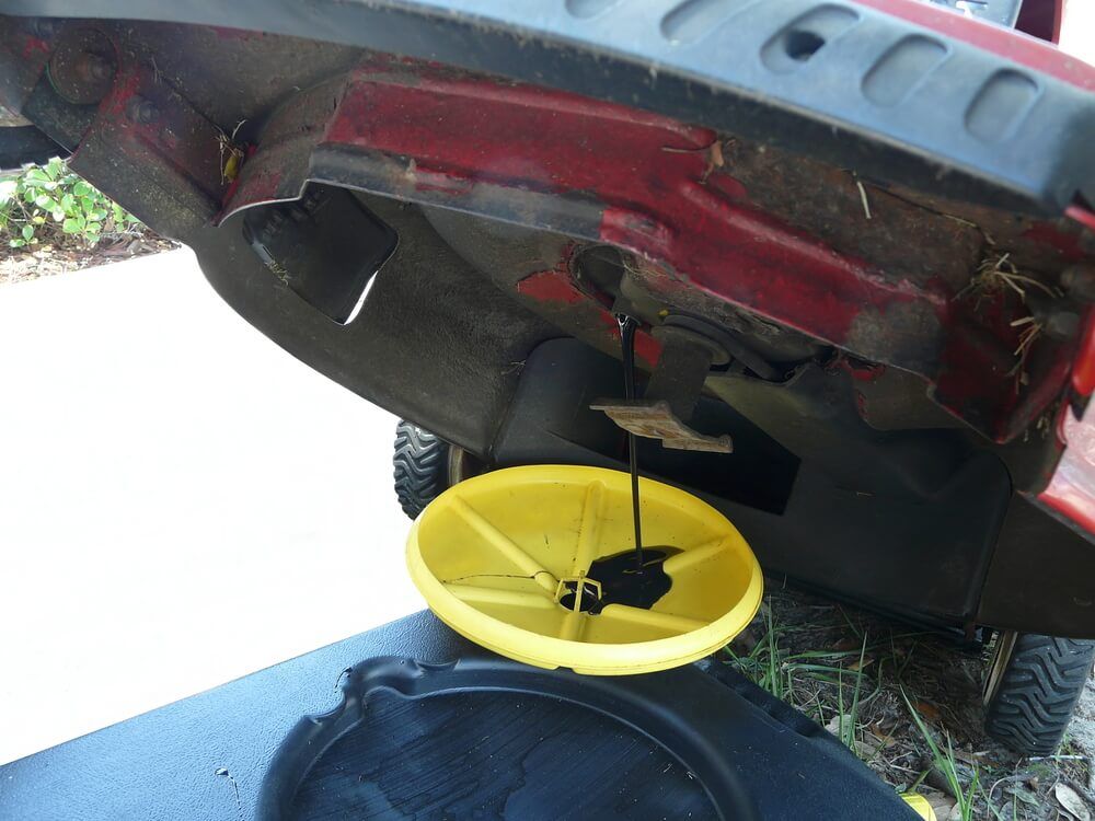 lawnmower oil draining into a black and yellow container. What to do when you have too much oil in lawn mower