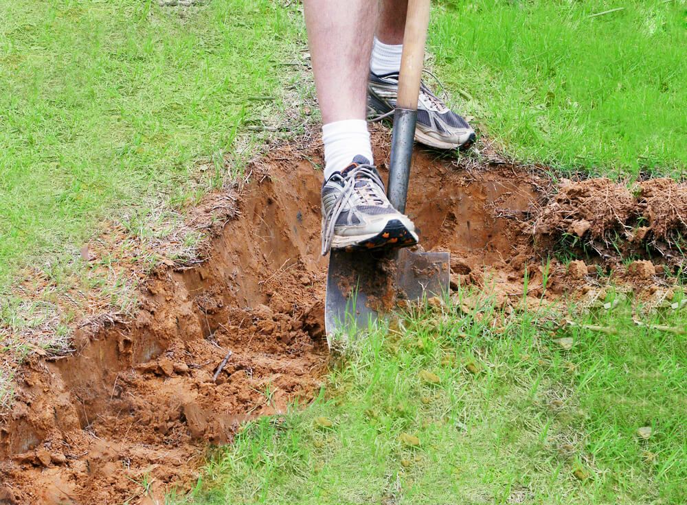man digging a hole with a garden shovel in the thick clay soil