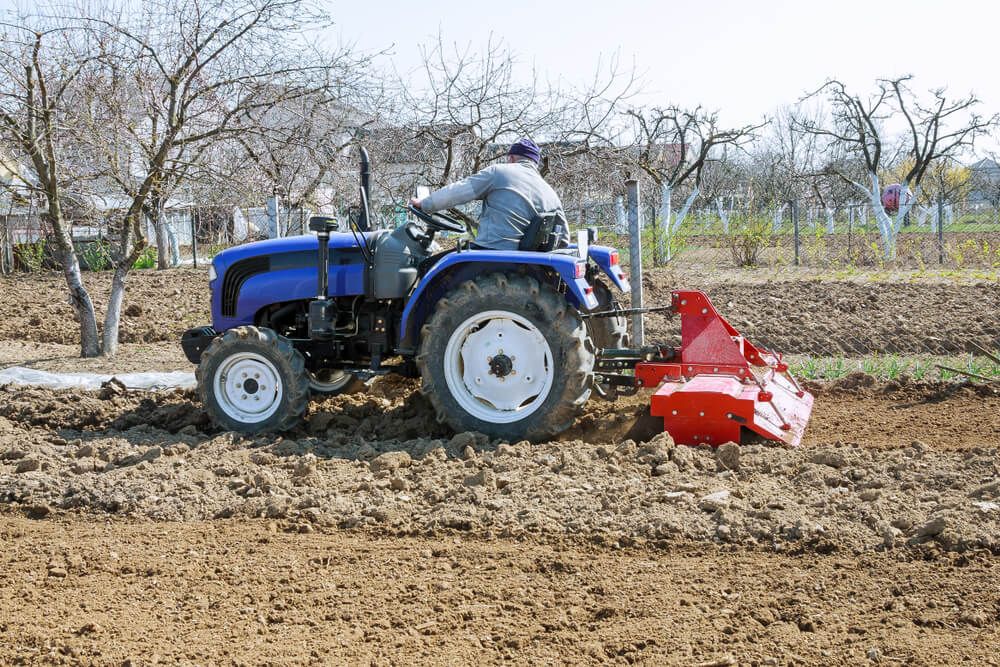 small farmyard tractor plowing the field with attachment