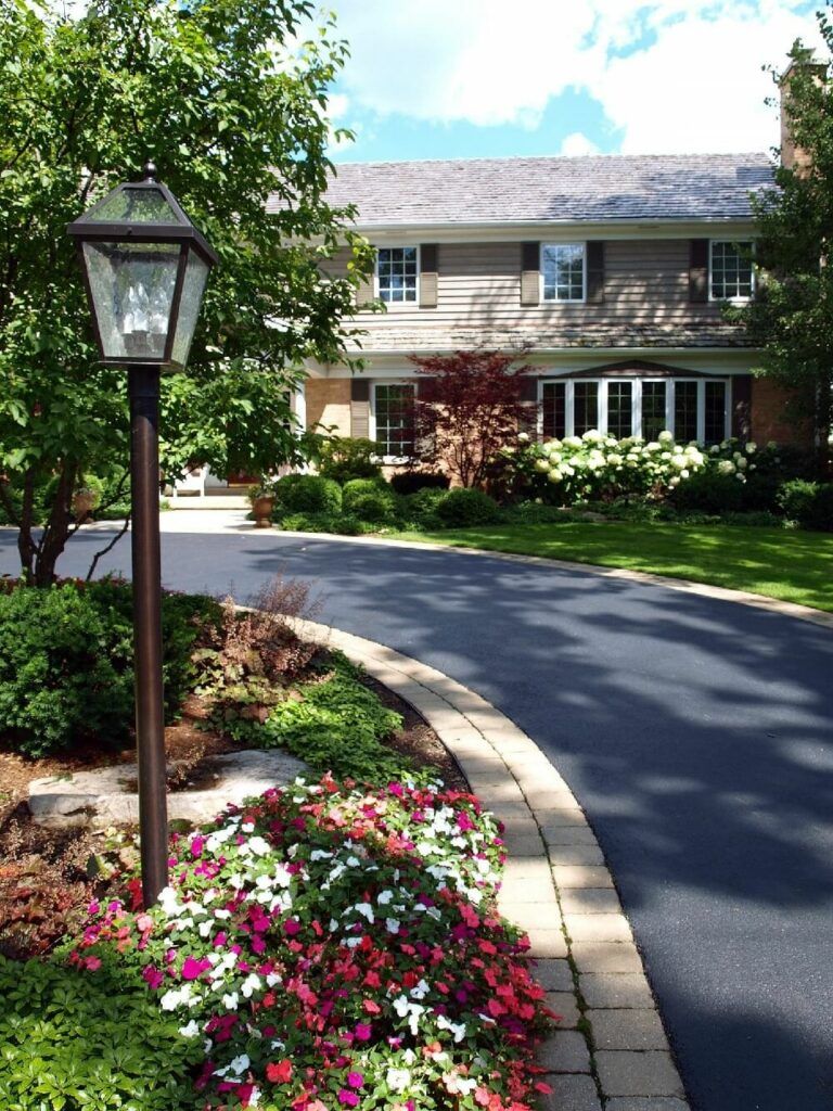 Fancy looking circular driveway design with lamp post and colorful flowers.